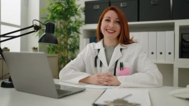 Young redhead woman wearing doctor uniform and medical mask working at clinic