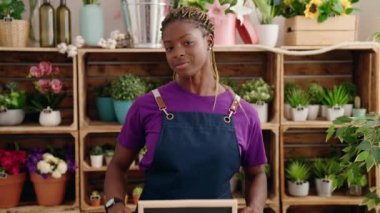 African american woman florist smiling confident holding open blackboard at florist