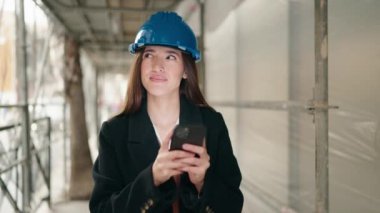 Young hispanic woman architect using smartphone at street
