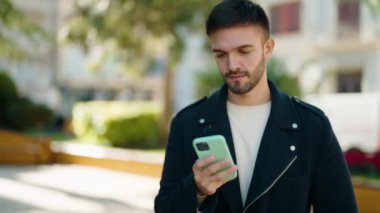 Young hispanic man using smartphone at park