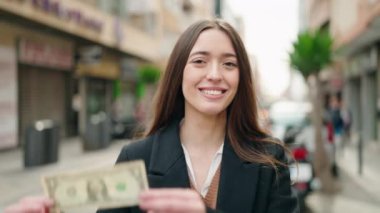 Young hispanic woman smiling confident holding dollar at street