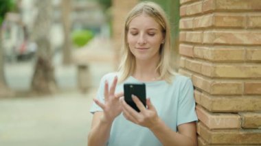 Sokakta akıllı telefon kullanan, kendine güvenen genç sarışın kadın.