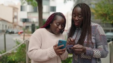 Two african american women using smartphone and credit card at street