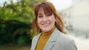 Orta yaşlı kadın yönetici parkta kendinden emin gülümsüyor.