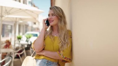 Gülümseyen genç bir kadın caddedeki akıllı telefondan konuşuyor.