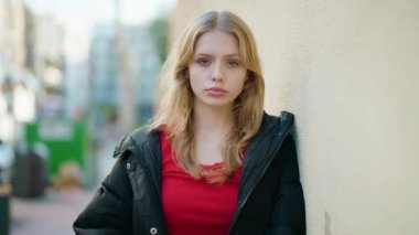 Young blonde girl with serious expression standing at street