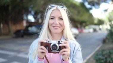 Young blonde woman tourist using vintage camera at street