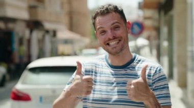 Young hispanic man smiling confident doing ok sign with thumbs up at street