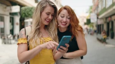 Two women standing together using smartphone at street