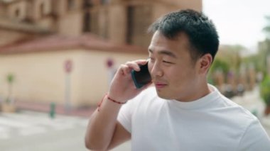 Genç Çinli adam gülümsüyor. Kendine güveni tam. Sokakta akıllı telefondan konuşuyor.