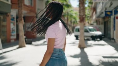 Afro-Amerikalı kadın gülümsüyor. Kollarını kavuşturup caddede duruyor.