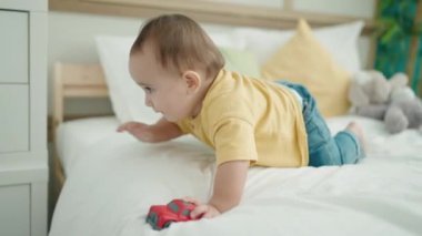Adorable hispanic baby playing with car crawling on bed at bedroom