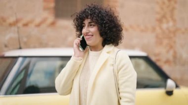 Gülümseyen genç bir kadın caddedeki akıllı telefondan konuşuyor.