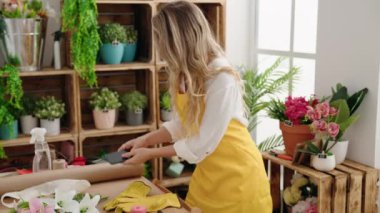 Young blonde woman florist smiling confident talking on smartphone at park