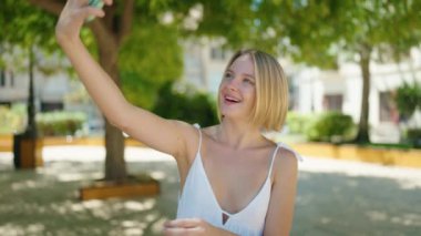 Parktaki akıllı telefonun yanında kendinden emin gülümseyen genç sarışın kadın.