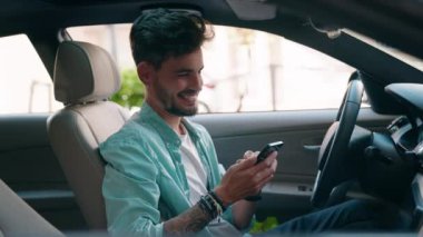 Young hispanic man using smartphone sitting on car at street