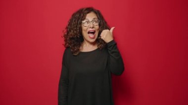 Middle age woman smiling confident pointing with fingers to the side over red background