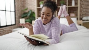 African american woman reading book lying on bed at bedroom