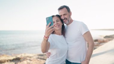 Erkek ve kadın çift birbirlerine sarılıyorlar. Deniz kenarındaki akıllı telefonun yanında selfie çekiyorlar.