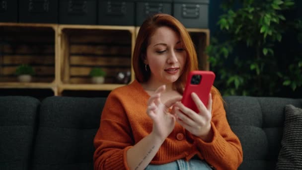 若い赤毛の女性は自宅でお祝いスマートフォンを使用して陽気に — ストック動画