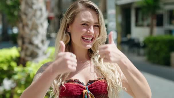 年轻的金发女人笑着自信地在街上竖起大拇指签个名 — 图库视频影像