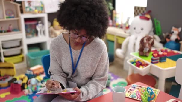 African American Woman Preschool Teacher Smiling Confident Writing Document Kindergarten — Vídeo de Stock