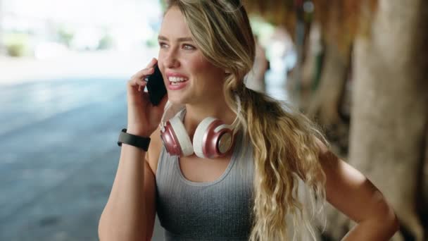 年轻的金发女人穿着运动服在街上用智能手机说话 — 图库视频影像