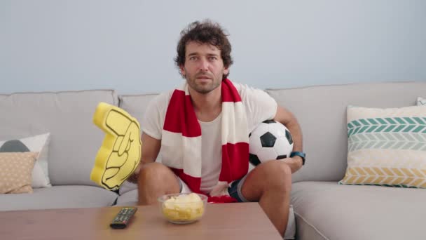 Młody Hiszpan Wspierający Drużynę Piłki Nożnej Siedzącą Kanapie Domu — Wideo stockowe