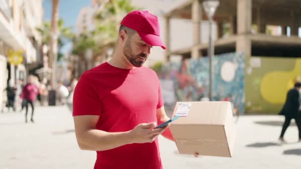 Νέοι Ισπανόφωνοι Deliveryman Κρατώντας Πακέτο Χρησιμοποιώντας Smartphone Στο Δρόμο — Αρχείο Βίντεο