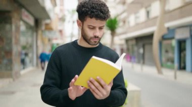 Sokakta kitap okuyan rahat ifadeli genç bir Arap.