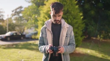 Young hispanic man standing with serious expression using camera at park