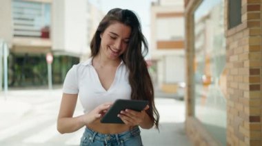 Young hispanic woman smiling confident using touchpad walking at street