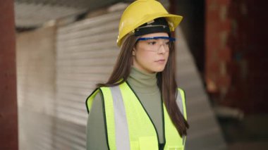 Young hispanic woman architect standing with serious expression at construction site