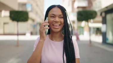 Afro-Amerikalı kadın gülümsüyor. Akıllı telefondan konuşuyor.