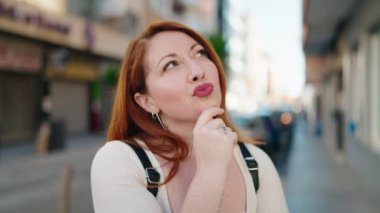 Young redhead woman with doubt expression standing at street