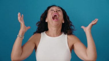 Middle age woman standing with surprise expression over isolated blue background