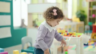 Adorable hispanic girl playing with construction blocks standing at kindergarten