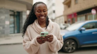 Afro-Amerikalı kadın sokakta akıllı telefon kullanarak kendine güveniyor.