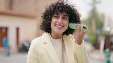 Caddedeki akıllı telefondan kendine güveni tam bir sesli mesaj dinleyen genç bir kadın.