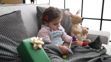 Adorable hispanic girl playing with hoops game sitting on sofa by christmas tree at home