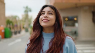 Young hispanic woman smiling confident looking to the sky at street