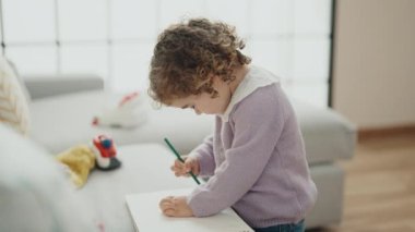 Adorable hispanic girl drawing on notebook standing at home