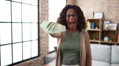 Middle age hispanic woman holding dollars banknotes