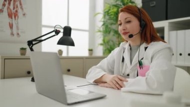Young redhead woman wearing doctor uniform having telemedicine at clinic