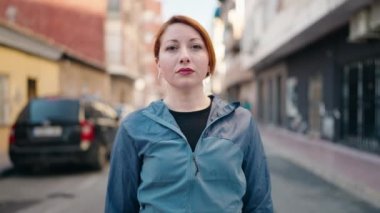 Young redhead woman wearing sportswear standing with arms crossed gesture at street