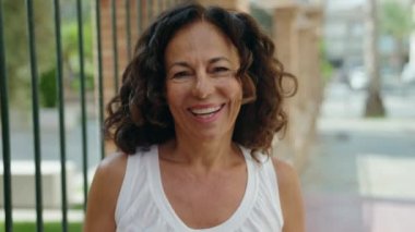 Orta yaşlı bir kadın sokakta kendine güvenerek gülümsüyor.