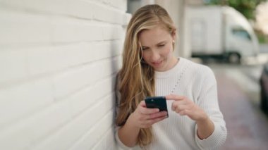 Sokakta akıllı telefon kullanan, kendine güvenen genç sarışın kadın.