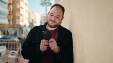 Young plus size man smiling confident using smartphone at street