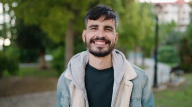 Genç İspanyol adam parkta yürürken kendinden emin gülümsüyor.