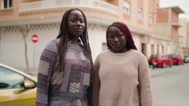 Two african american women smiling confident standing with arms crossed gesture at street